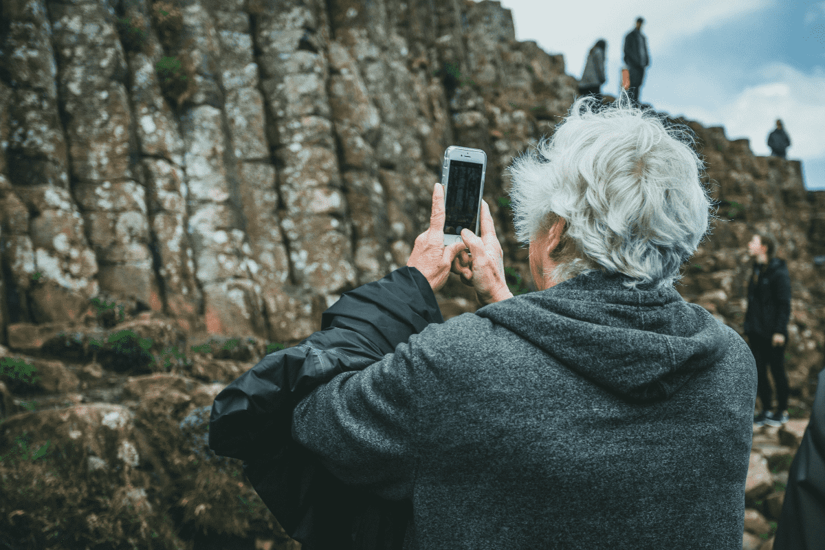 A senior takes a picture with their mobile phone during a hike.